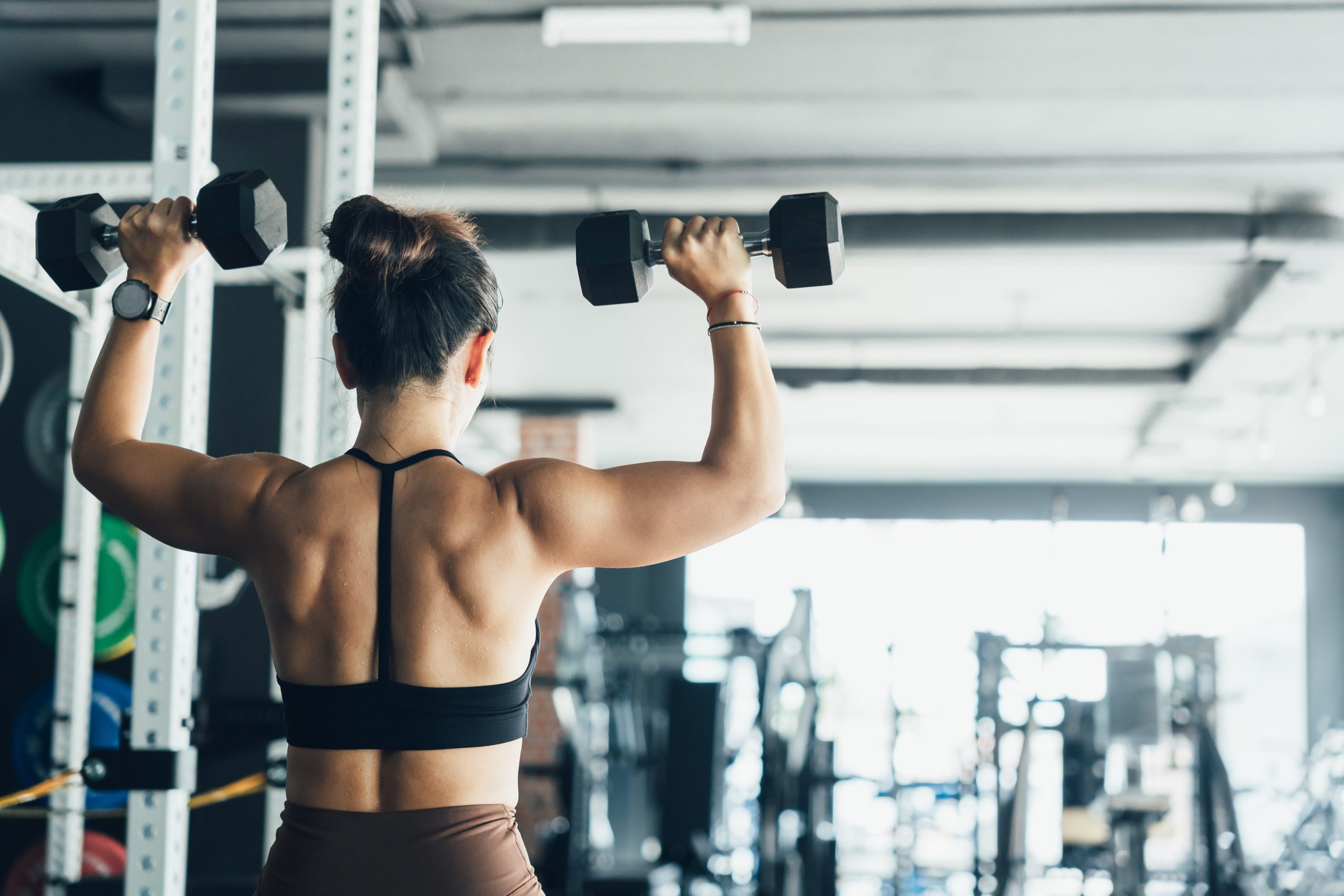 Woman lifting weights in a gym while focusing on strength training and fitness during afternoon workout
